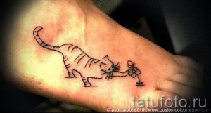 Фото тату на стопе: маленький котенок с забавным выражением морды держит в лапках нежный цветок. Черно-белый рисунок татуировки.