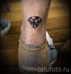 Фото тату: небольшой черный бриллиант, выполненный в графичном стиле, на лодыжке. Простой и элегантный рисунок татуировки.