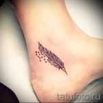 Фото тату перо на лодыжке. Татуировка выполнена в черном цвете с детальной проработкой текстуры пера и небольшими точками вокруг.
