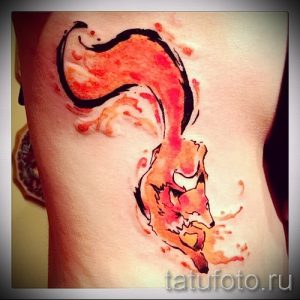 Фото тату лисы, выполненной в технике акварели на боку. Рисунок с плавными переходами цветов и эффектом размытости.