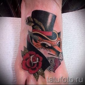 Фото тату лисы в цилиндре с розой на стопе. Рисунок татуировки в стиле traditional с использованием ярких цветов.