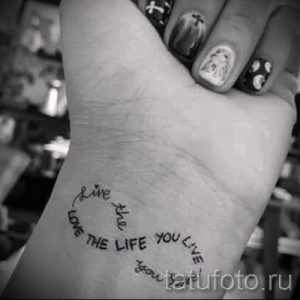 Фото тату бесконечности, выполненной в виде круга с надписью 'Love the life you live', на руке. Простой и элегантный дизайн, символизирующий позитивное отношение к жизни.
