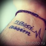 Фото тату надписи 'nasci assim' на запястье, выполненной черными чернилами в стиле леттеринг с добавлением изображения пульса.