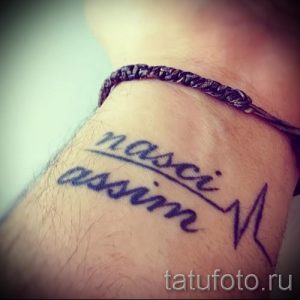 Фото тату надписи 'nasci assim' на запястье, выполненной черными чернилами в стиле леттеринг с добавлением изображения пульса.