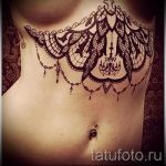 Фото тату: сложный узор кружева украшает грудь и живот девушки. Детализированный рисунок татуировки в черно-белых тонах с элементами люстры.
