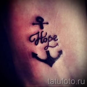 Фото тату: маленькая татуировка на коже, изображающая якорь и надпись "Hope". Морская тематика, минимализм, надежда.