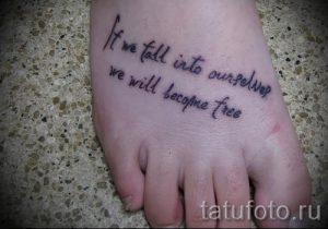 Фото тату с надписью "If we fall into ourselves we will become free" на стопе, выполненное черными чернилами. Рисунок выполнен каллиграфическим шрифтом. Эскиз татуировки выглядит вдохновляюще и мотивирующе.