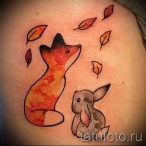 Фото простой татуировки лисы и зайца, окруженных падающими листьями, выполненной в минималистичном стиле.