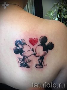 Фото тату на лопатке с изображением Микки и Минни Маус, целующихся. Яркий красный сердечко добавляет романтичности рисунку.