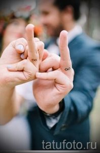 Фото тату бесконечности на безымянных пальцах пары, символизирующих вечную любовь и связь. Минималистичный дизайн, выполненный черными чернилами.