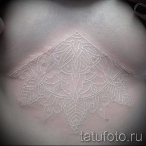 Фото тату: большая белая мандала, расположенная на груди, создающая эффект воздушного кружева на коже.