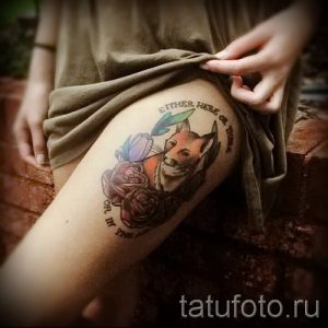 Фото акварельной татуировки лисы с цветами и надписью на бедре. Мягкие переходы цветов и нежные детали.