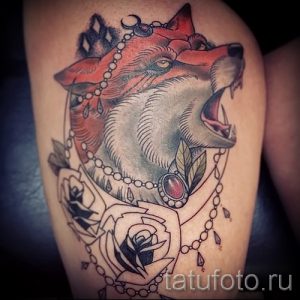 Фото тату волчьей головы в стиле олд скул с ожерельем из драгоценных камней и окруженной розами на плече.