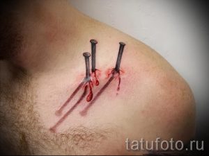 Фото реалистичной татуировки на плече: три гвоздя, вбитых в кожу, с капающей кровью. Детализированный рисунок, мрачная тематика.