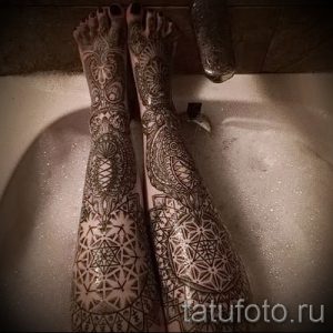 Фото тату: сложный рисунок в стиле мехенди, покрывающий ноги и ступни, выполненный в теплых коричневых тонах.