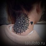 Фото татуировки мандалы на затылке девушки, дополненной небольшим сердечком. Изящный рисунок в черных тонах.