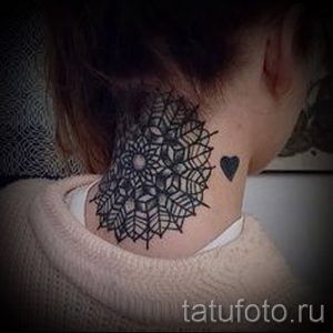 Фото татуировки мандалы на затылке девушки, дополненной небольшим сердечком. Изящный рисунок в черных тонах.