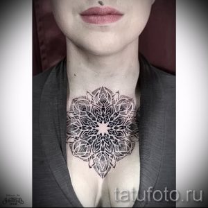 Фото тату: большая черно-белая мандала, выполненная в технике дотворк, украшает шею и верхнюю часть груди. Детализированный рисунок с использованием точек разного размера.