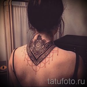 Фото тату: черная мандала с красными точками на спине девушки. Детализированный рисунок татуировки с геометрическими узорами и тонкими линиями.