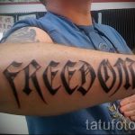 Фото тату: надпись "FREEDOM" выполнена черным цветом на предплечье в готическом стиле. Буквы имеют острые углы и декоративные элементы.