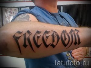Фото тату: надпись "FREEDOM" выполнена черным цветом на предплечье в готическом стиле. Буквы имеют острые углы и декоративные элементы.