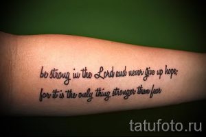 Фото тату: надпись "be strong in the Lord and never give up hope, for it is the only thing stronger than fear" выполнена черным цветом на предплечье.