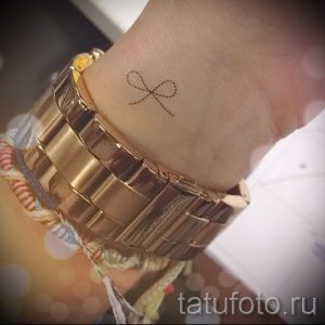 Фото тату: Маленький бантик, выполненный в коричневых тонах, на женском запястье. Элегантный и сдержанный рисунок татуировки.