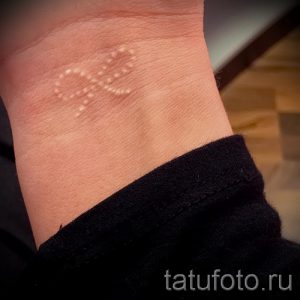 Фото тату: Изящный белый бантик, выполненный техникой white ink, на женском запястье. Необычный и стильный рисунок татуировки.