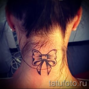 Фото тату черного банта на задней части шеи. Простой и элегантный рисунок татуировки, выполненный в технике контурной графики.