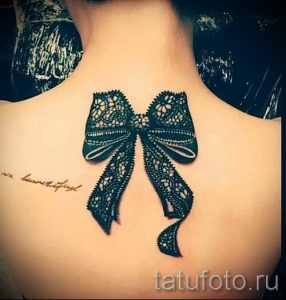 Фото тату большого черного банта из кружева на спине. Детализированный рисунок татуировки, выполненный в реалистичном стиле с использованием теней и градиентов.