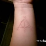 Фотография белой татуировки на запястье с изображением символа Даров Смерти из Гарри Поттера. Нежный и изящный рисунок татуировки.