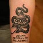 Фото тату на предплечье: Всевидящее око в треугольнике, обвитое змеей, с латинской надписью. Стильный и загадочный рисунок татуировки.