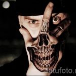 Фото тату на руке: реалистичный череп с открытым ртом и инициалами 'N' на пальце. Черно-белый рисунок татуировки, выполненный в мрачном стиле.