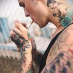 Фото татуировки на шее и руке мужчины: изображение девушки с сигаретой и татуировкой розы. Стиль - традиционный.