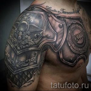 Фото тату на плече, изображающее рыцарские доспехи. Детализированный рисунок в реалистичном стиле, выполненный в черно-серых тонах.