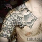 Фото тату: черно-серая татуировка на плече мужчины, изображающая рыцарские доспехи и кольчугу, выполненная в реалистичном стиле.