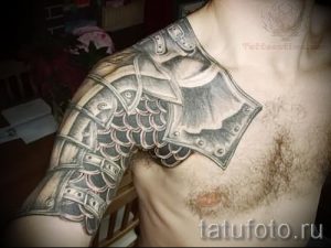 Фото тату: черно-серая татуировка на плече мужчины, изображающая рыцарские доспехи и кольчугу, выполненная в реалистичном стиле.