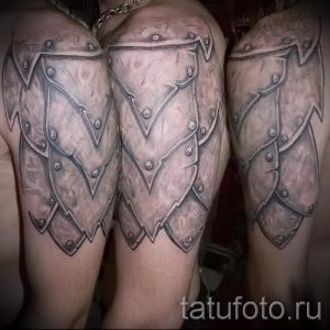Фото тату: реалистичное изображение металлических доспехов на плече, выполненное в серо-черной гамме с высокой детализацией и текстурой металла.