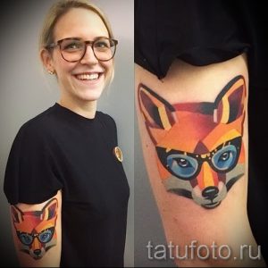 Фото татуировки лисы в очках, выполненной в геометрическом стиле. Яркие оранжевые и синие цвета, четкие линии.