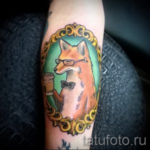 Фото татуировки лисы в очках и с галстуком-бабочкой, держащей чашку кофе. Стиль олдскул, яркие цвета.