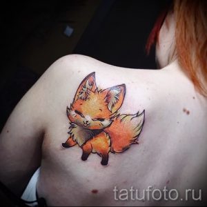 Фото тату маленького, очаровательного лисенка в мультяшном стиле, расположенного на женской лопатке. Нежный рисунок татуировки.