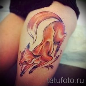 Фото тату лисы на бедре, выполненной в мягких тонах с плавными линиями. Рисунок изображает лису в изящной позе, с поднятым хвостом.