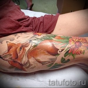 Фото тату лисы, лежащей среди цветов на руке. Изображение выполнено в ярких и насыщенных цветах, с акцентом на детализацию шерсти и лепестков цветов.