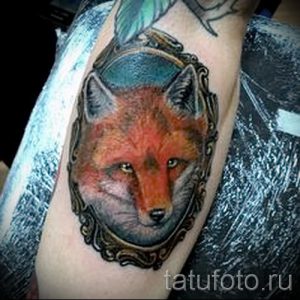 Фото тату лисы в старинной рамке на руке. Рисунок выполнен в реалистичном стиле с использованием коричневых, оранжевых и золотых оттенков. Оригинальный и стильный дизайн.