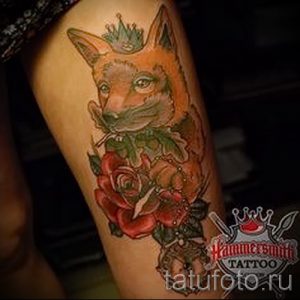 Фото тату лисы с розами и короной на бедре. Рисунок выполнен в ярких, насыщенных цветах с использованием оранжевого, красного и зеленого оттенков. Изысканный и женственный дизайн.