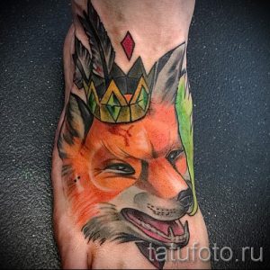 Фото тату лисы в короне на стопе. Рисунок выполнен в ярких, насыщенных цветах с использованием оранжевого, черного и зеленого оттенков. Стильный и оригинальный дизайн.