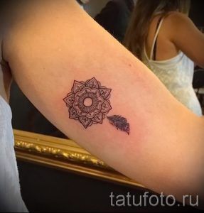 Фото тату: Небольшая коричневая мандала и перо на предплечье. Деликатный рисунок татуировки в минималистичном стиле.