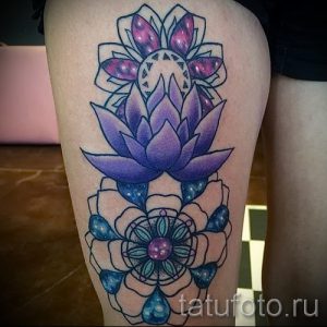 Фото татуировки лотоса на бедре, выполненной в ярких фиолетовых и синих тонах. Рисунок выглядит объемно и реалистично.