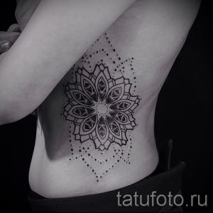 Фото тату: черная мандала с точками и геометрическими узорами, расположенная на боку. Детализированный рисунок татуировки.