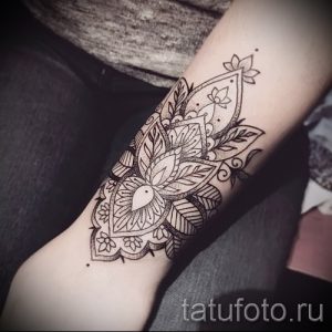 Фото тату: черная мандала с цветочными элементами, расположенная на предплечье. Детализированный рисунок татуировки в стиле дотворк.